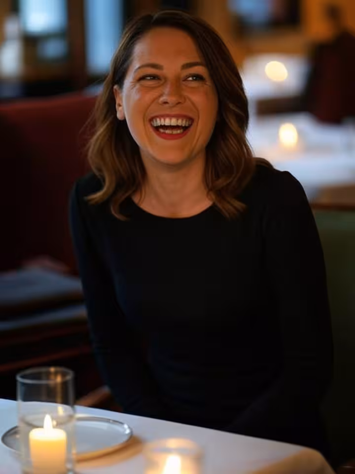 profile portrait of woman in classic black dress laughing genuinely while sitting at upscale restaur